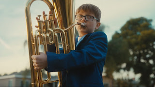 A boy enlists a tuba in a quixotic quest to woo the girl of his dreams in the heartwarming short film Mariachi Boy, directed by Michael Gabriele and produced by Daily Planet. Proving the timeless maxim that love conquers all, the film follows the boy as he repeatedly shows up in the front yard of a cute Hispanic girl and tries to serenade her. His mangled attempt to perform a mariachi tune on his bulky instrument perplexes the girl and annoys her father. Ultimately, the boy’s dad comes to his rescue by rounding up a troop of professional mariachi musicians to provide backup.